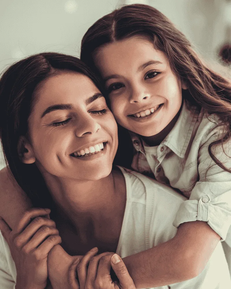 A mother and her daughter together, the daughter's arms around her, both smiling